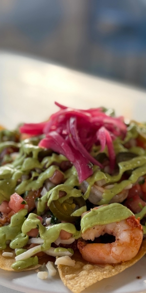 Fresh shrimp nachos topped with avocado sauce, pico de gallo, jalapeños, and pickled onions at Makai Seafood Market in San Diego.