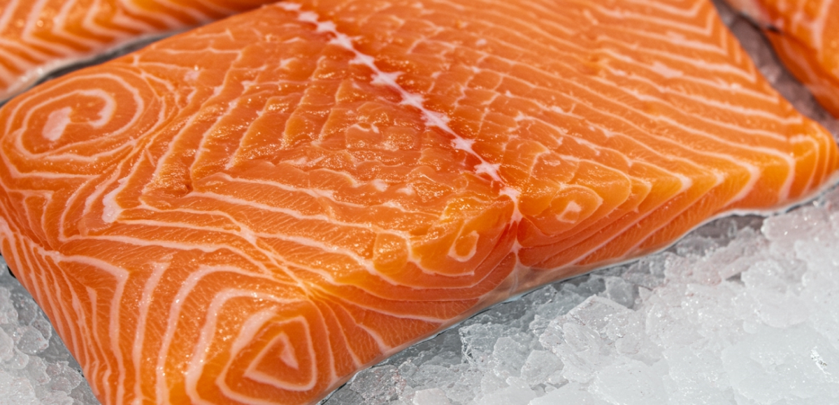 Close-up of raw salmon fillets on crushed ice, detailed marbling and bright orange color under natural daylight, seafood counter style.