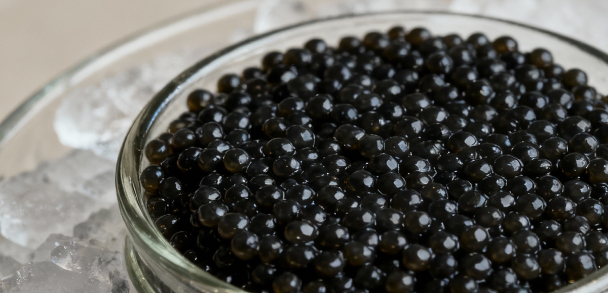 Glass bowl of premium black caviar over crushed ice, shiny texture pearls with elegant neutral background and cinematic soft lighting.